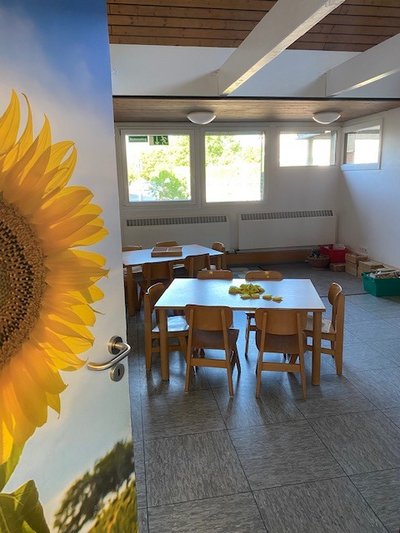 Tür mit Sonnenblume, Blick in Raum mit Gruppen-Tischen und Stühlen